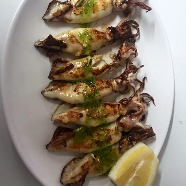Calamares a la plancha con perejil y una cuña de limón en plato ovalado