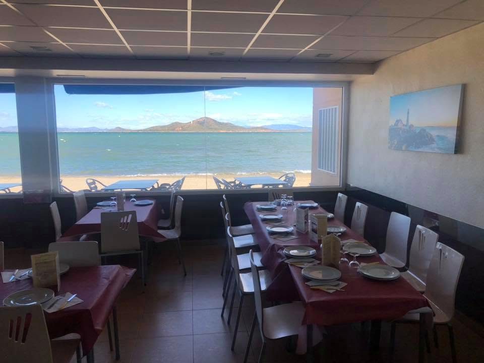 Comedor con mesas vestidas y un ventanal corrido que da a la playa y a la isla