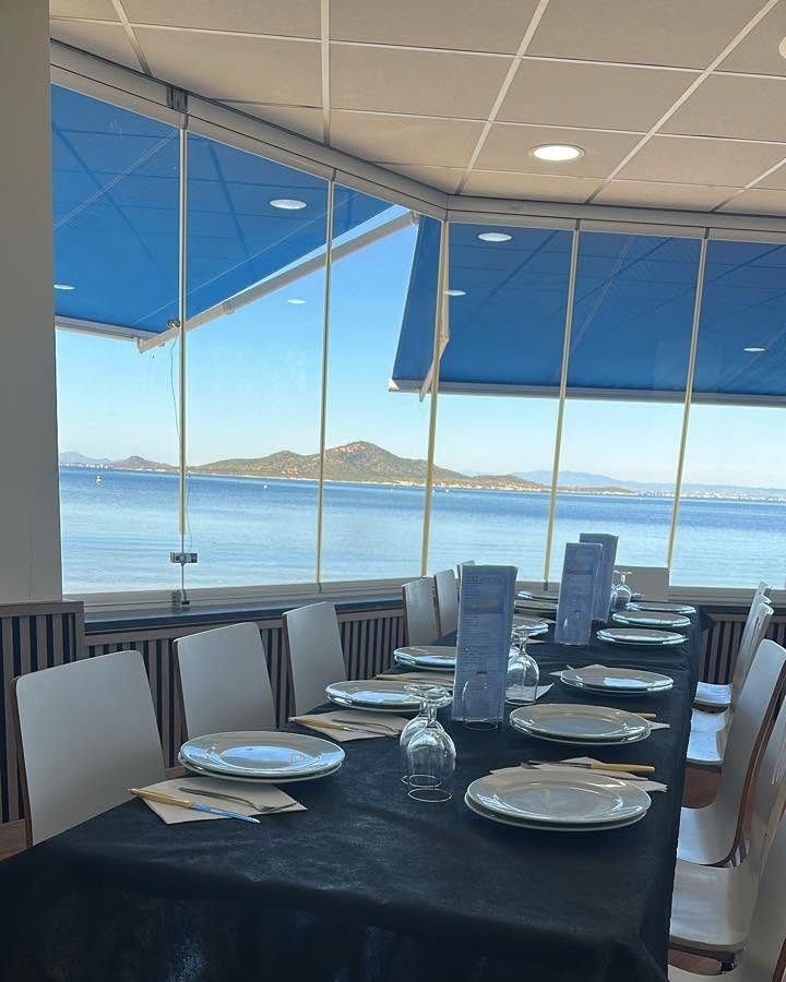 Mesa larga puesta junto al ventanal del comedor, con la isla al fondo sobre el agua