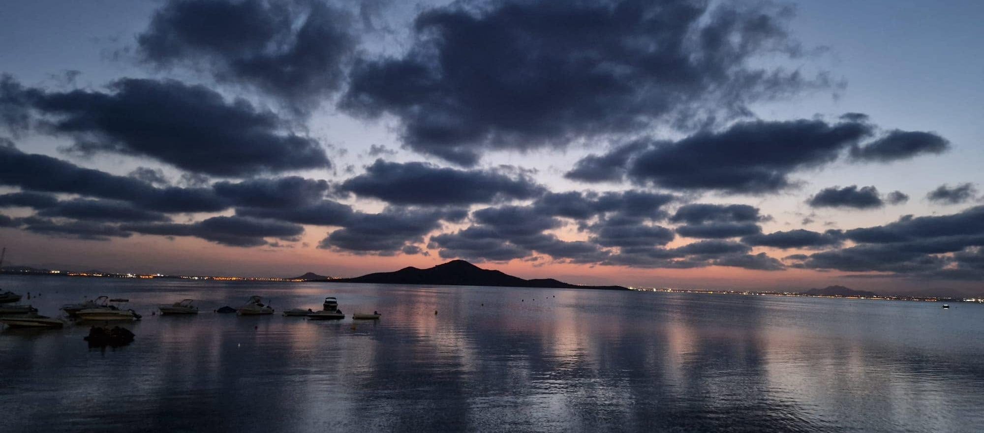 La Isla del Barón recortada sobre el Mar Menor al atardecer, con barcas fondeadas cerca de la orilla