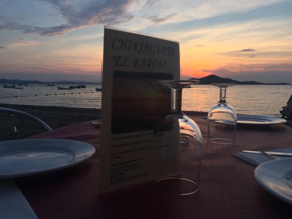 Mesa de la terraza puesta al atardecer, con la carta de la casa y la isla al fondo