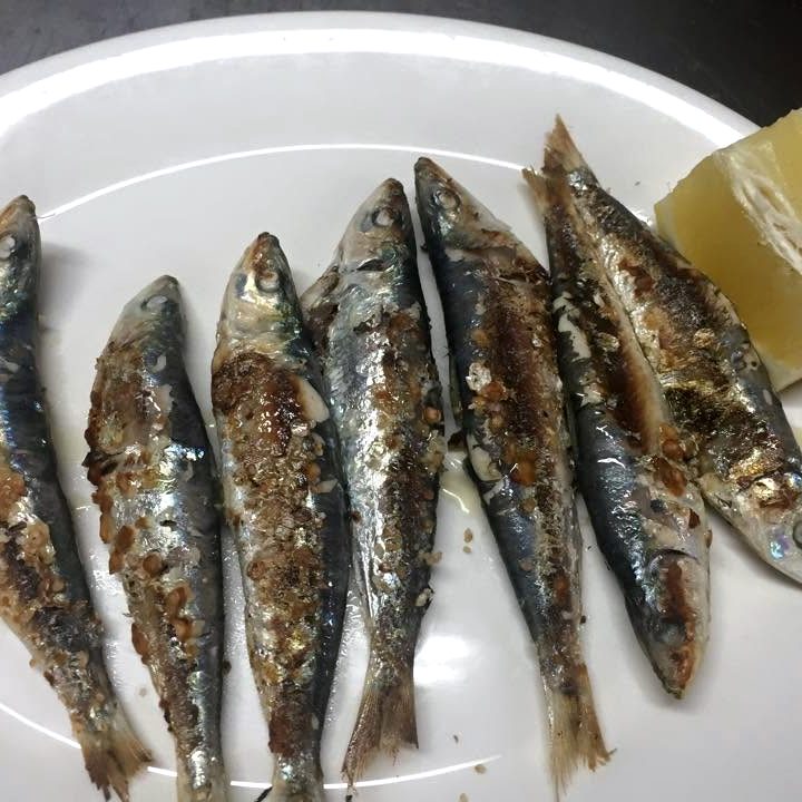 Ocho sardinas a la plancha ordenadas en un plato blanco, con limón